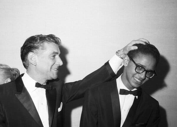 A black-and-white photo of a very young Mr. Watts with Leonard Bernstein. They are both wearing tuxedos, and Mr. Bernstein has his left hand on top of a smiling Mr. Wattss head.